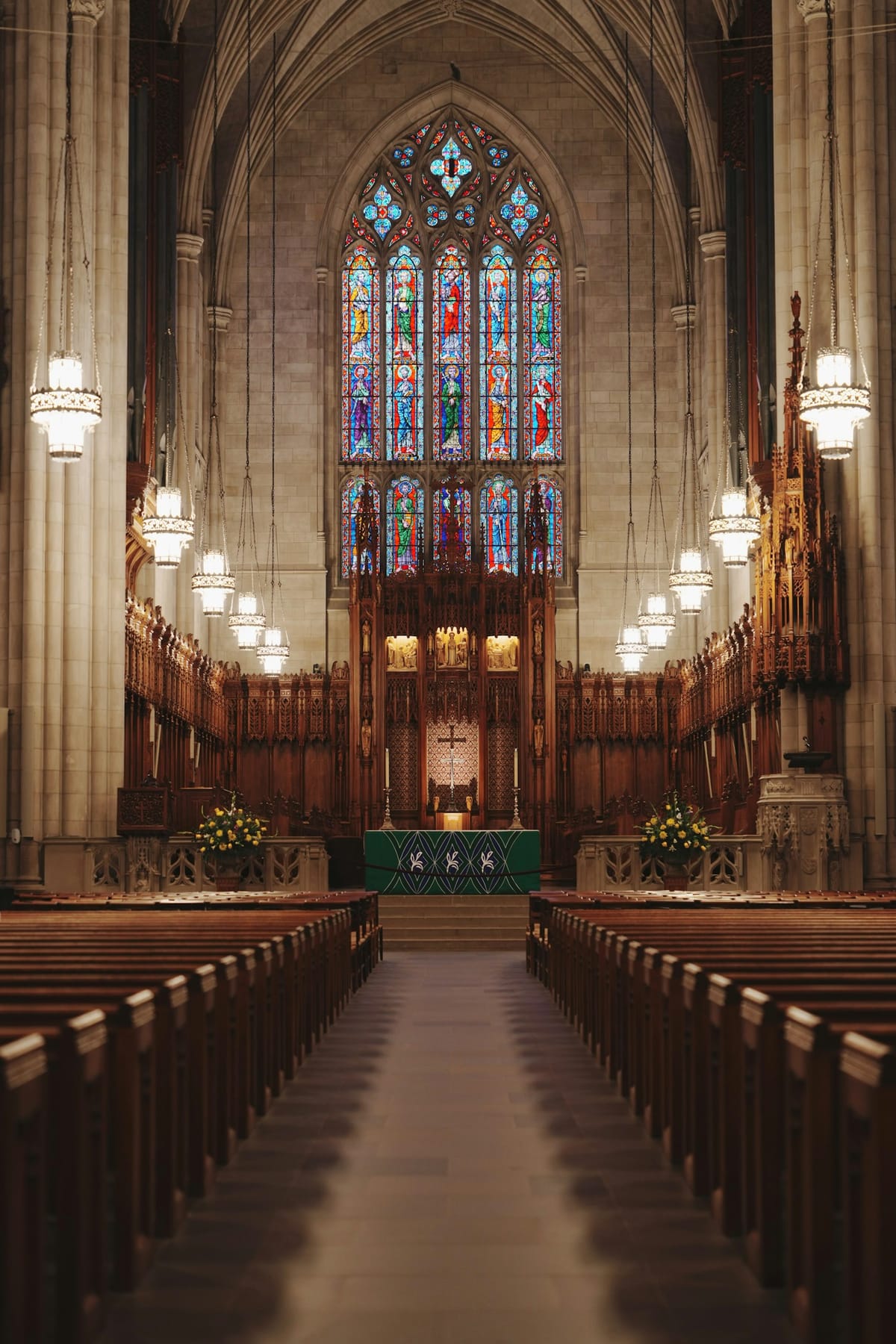A tall sanctuary with rows of wooden pews under a stained glass window